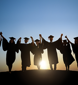 Graduates hold hands on a hill as the sun rises